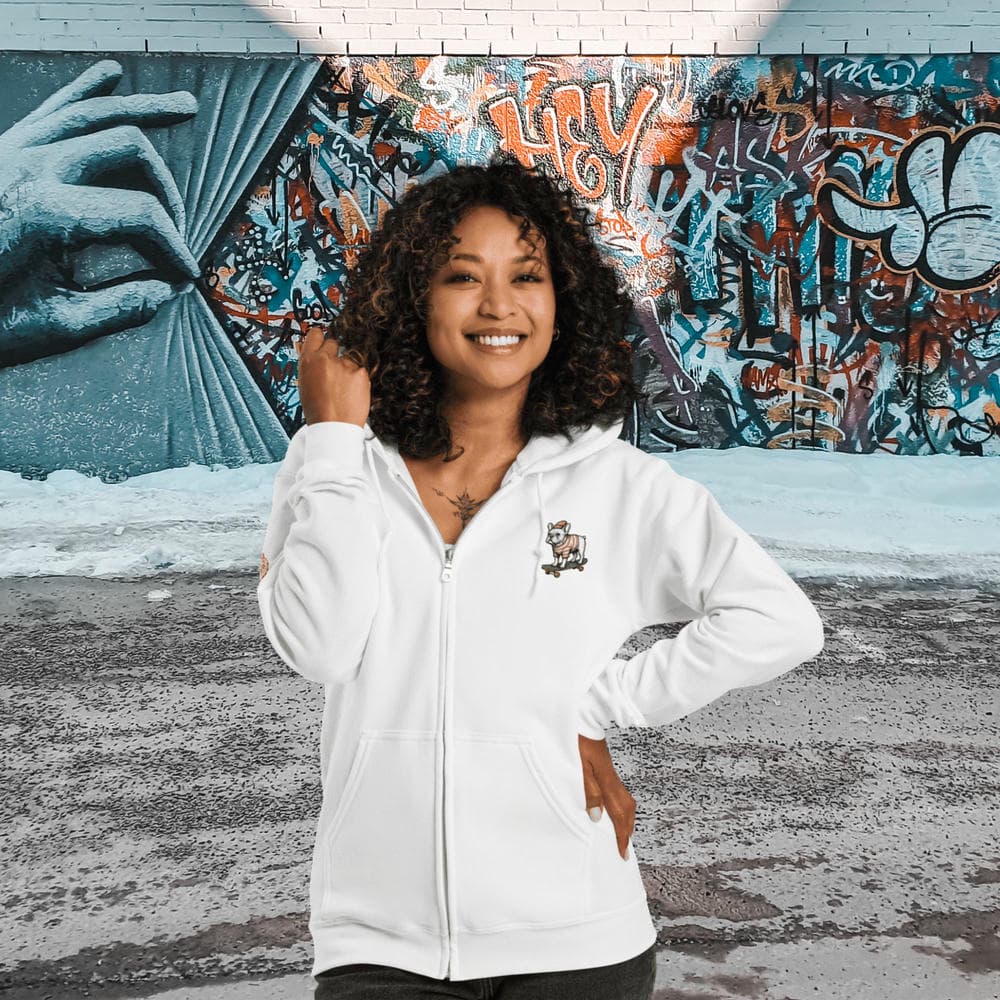 Vue de face d'une femme portant le Hoodie Zippé Alpha blanc Bouledogue De Rue devant un mur de briques orné de graffitis. Design artistique intégral en matière bio premium avec une illustration de bouledogue, arborant le Sceau de la Meute exclusif à la marque Felpatee.