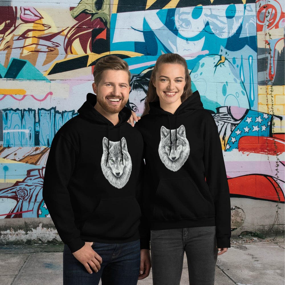 Vue de face d'un homme et d'une femme portant le Hoodie Essentiel noir Instinct Émeraude devant un mur de briques recouvert de graffitis colorés. Design by Mister Felpatee placé sur la poitrine pour un style urbain dynamique signé Felpatee.