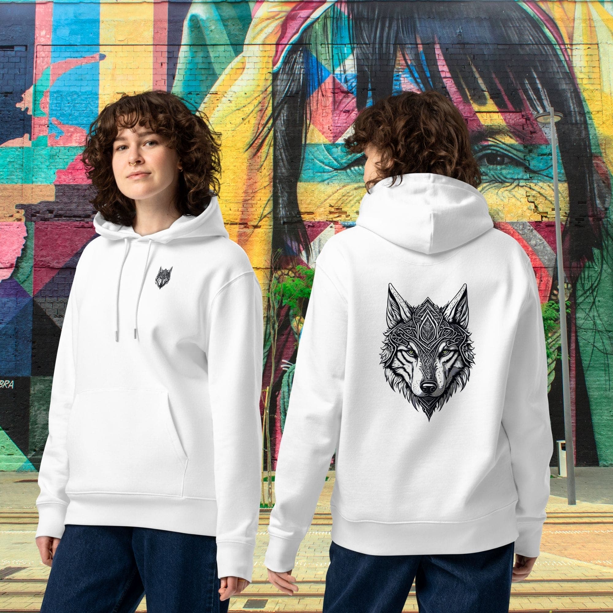 Mise en situation urbaine montrant les vues face et dos du hoodie Prestige blanc. Le design Loup Gardien Runique 360° ressort devant un mur de briques tagué.