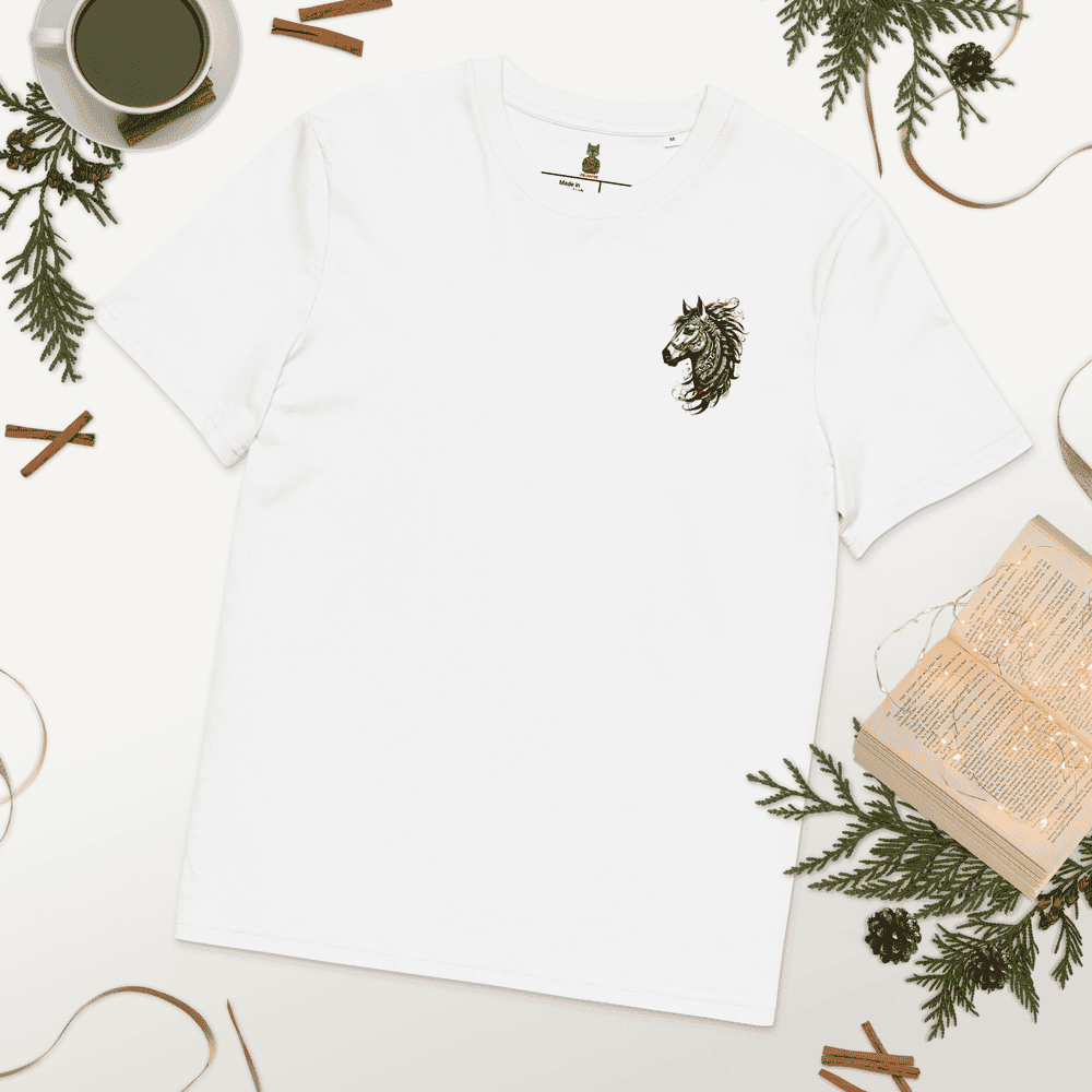 Flat lay (vue à plat) du T-shirt Exception blanc au design minimaliste Esprit Tribal Équin. Il est entouré de décorations de Noël nature : branches de sapin, bâtons de cannelle et un livre ouvert. Collection de fêtes Mister Felpatee.