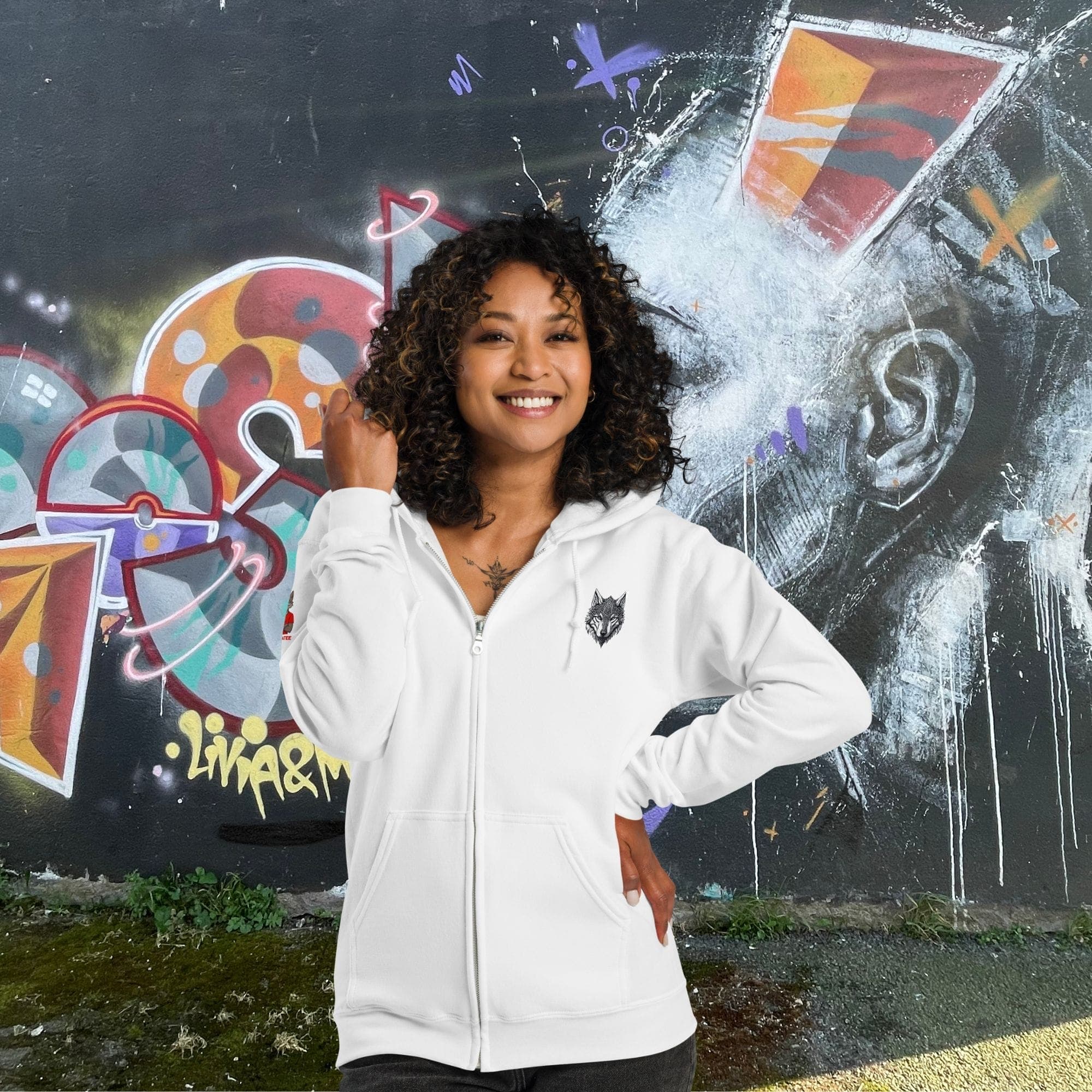 Femme portant le hoodie zippé Alpha blanc avec design Loup Gardien Runique 360°, posant devant un mur urbain coloré. Style exclusif Mister Felpatee.