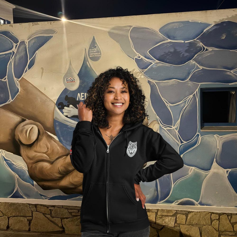 Vue de face d'une femme portant le Hoodie Zippé Alpha noir Instinct Émeraude devant un mur streetwear. Design artistique intégral en matière premium, arborant le Sceau de la Meute, symbole de l'exclusivité by Mister Felpatee.